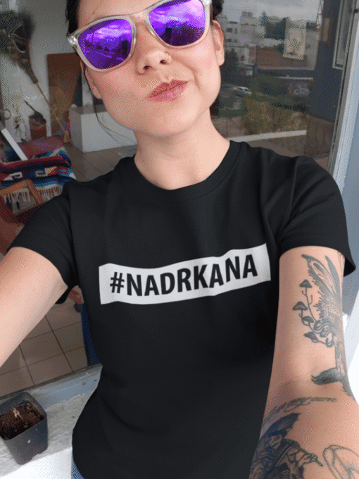 1. Ženska u crnoj majici s natpisom #NADRKANA, odraz grada u naočalama.