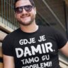 Nasmiješeni muškarac u crnoj majici s textom na hrvatskom, na otvorenom prostoru.