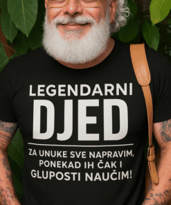 Otvoren smiješak starijeg muškarca s naočalama i šalom, u crnoj majici s natpisom, outdoor okruženje sa zelenim lišćem.