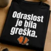 Crna majica s natpisom Odraslost je bila greška. s malim razbijenim kasicom-prasicom u minimalističkom dizajnu